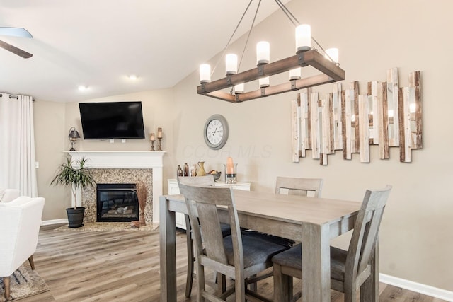 dining space featuring vaulted ceiling, a ceiling fan, wood finished floors, a glass covered fireplace, and baseboards