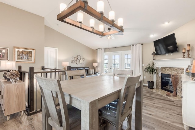 dining area with light wood finished floors, a high end fireplace, and lofted ceiling