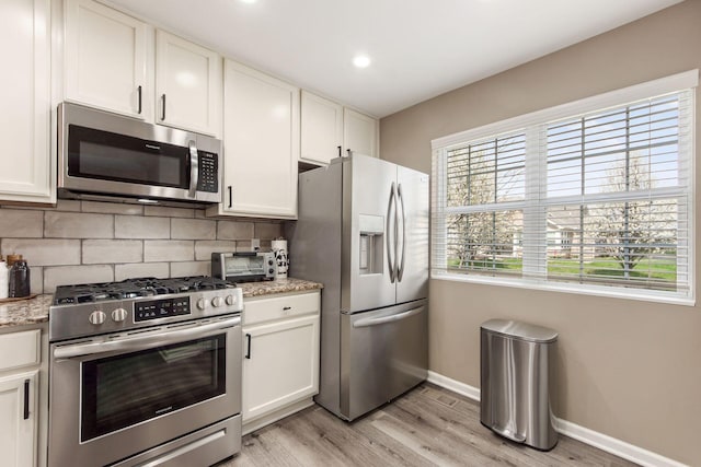 kitchen featuring tasteful backsplash, light wood-type flooring, white cabinets, baseboards, and appliances with stainless steel finishes