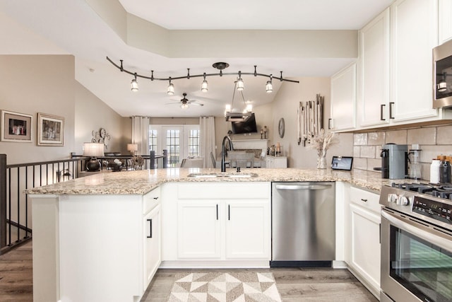 kitchen featuring stainless steel appliances, a peninsula, a sink, white cabinetry, and light stone countertops