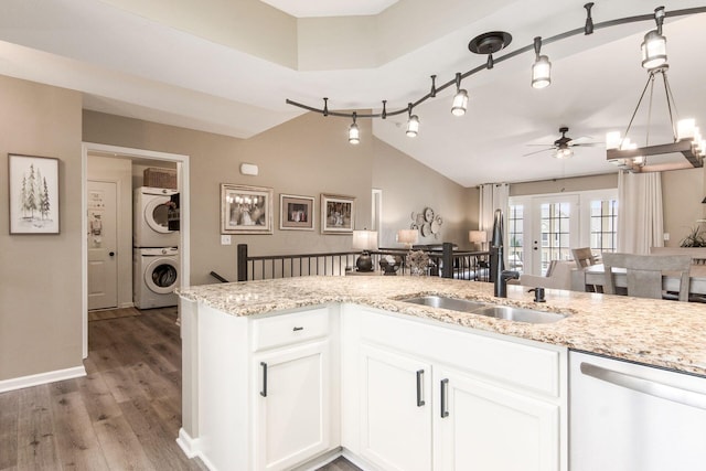 kitchen featuring stacked washer and clothes dryer, vaulted ceiling, stainless steel dishwasher, light wood-style floors, and ceiling fan