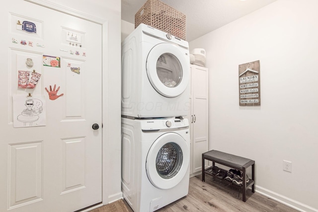laundry room with baseboards, stacked washer and clothes dryer, light wood-style floors, and laundry area
