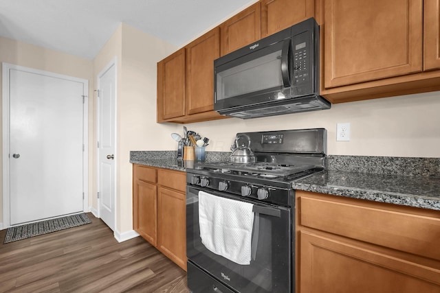 kitchen featuring dark wood-style flooring, brown cabinetry, black appliances, and dark stone countertops