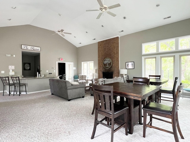 dining area featuring light carpet, a fireplace, high vaulted ceiling, a ceiling fan, and visible vents