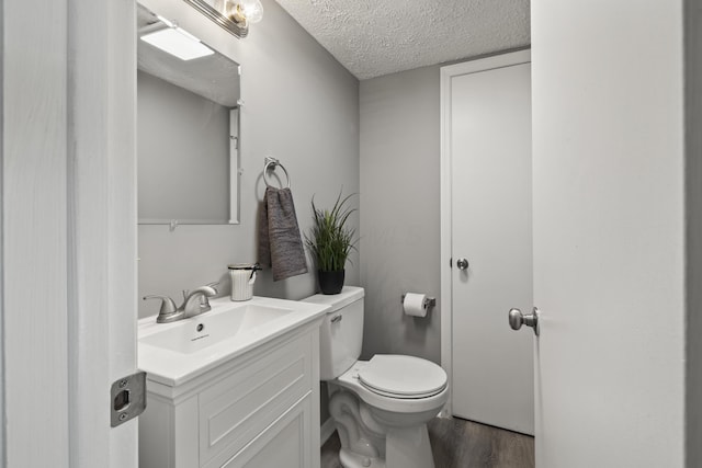 bathroom with wood finished floors, a textured ceiling, toilet, and vanity