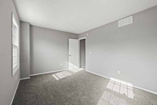 unfurnished bedroom with a textured ceiling, visible vents, carpet flooring, and baseboards