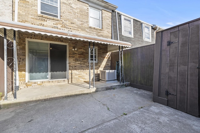 rear view of house featuring brick siding, central AC unit, fence, and a patio area