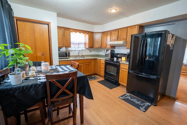kitchen with under cabinet range hood, light countertops, a sink, light wood-style floors, and black appliances