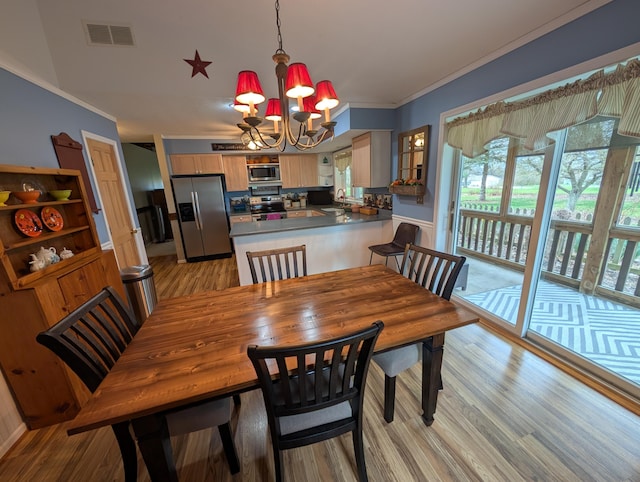 dining space with a chandelier, light wood finished floors, visible vents, and ornamental molding