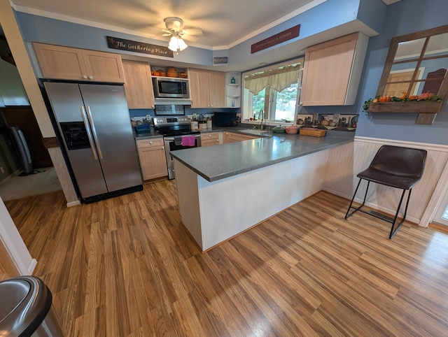 kitchen featuring light brown cabinets, a peninsula, dark countertops, stainless steel appliances, and a sink