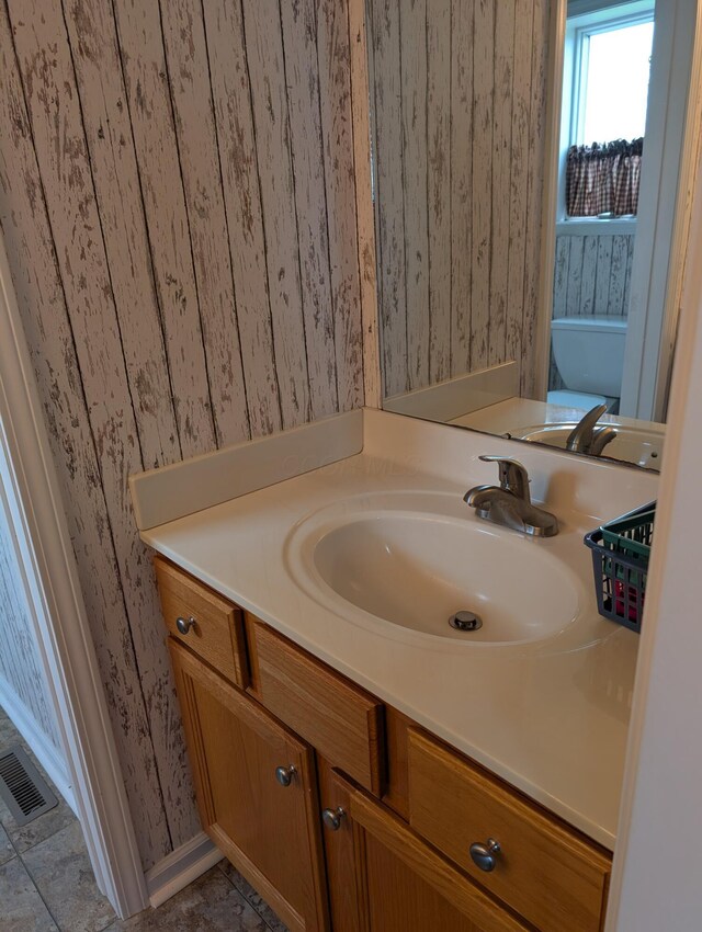 bathroom with wallpapered walls, vanity, baseboards, and visible vents