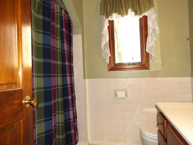 bathroom with tile walls, a wainscoted wall, vanity, and toilet