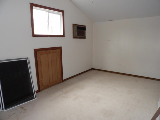 spare room with an AC wall unit, baseboards, light colored carpet, and lofted ceiling
