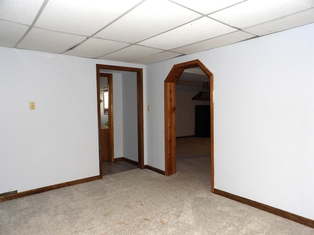unfurnished room featuring light colored carpet, arched walkways, baseboards, and a drop ceiling