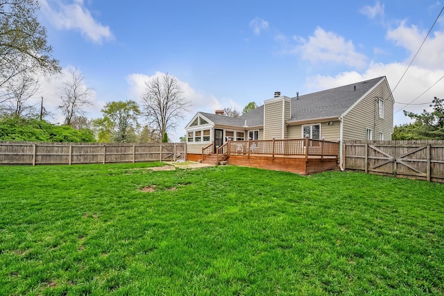 back of property featuring a chimney, a wooden deck, a gate, a fenced backyard, and a yard