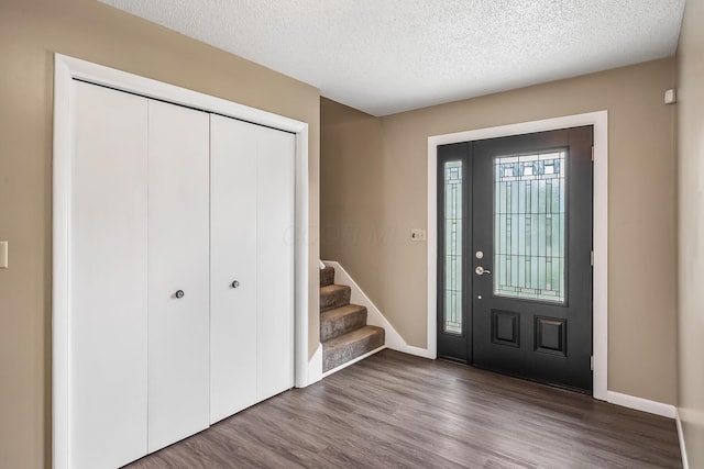 foyer featuring stairs, a textured ceiling, baseboards, and wood finished floors