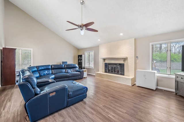 living room with ceiling fan, a brick fireplace, high vaulted ceiling, baseboards, and wood finished floors