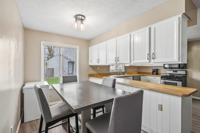 kitchen featuring wooden counters, a textured ceiling, appliances with stainless steel finishes, wood finished floors, and a sink