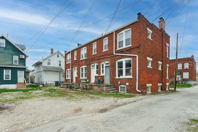 townhome / multi-family property featuring brick siding, central AC unit, and a chimney