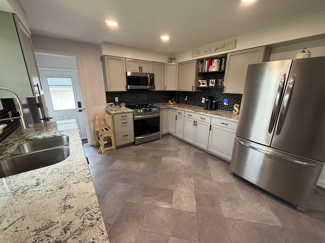kitchen featuring stainless steel appliances, a sink, tasteful backsplash, open shelves, and light stone countertops
