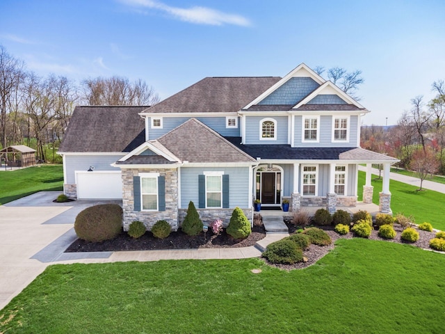 craftsman-style house featuring a shingled roof, concrete driveway, covered porch, stone siding, and a front yard
