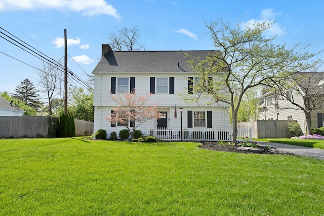 colonial-style house with a chimney, fence, a front lawn, a porch, and roof with shingles
