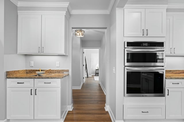 kitchen featuring dark stone countertops, stainless steel double oven, white cabinetry, baseboards, and ornamental molding