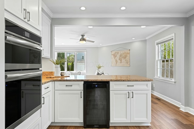 kitchen with light stone countertops, a healthy amount of sunlight, stainless steel double oven, and wine cooler