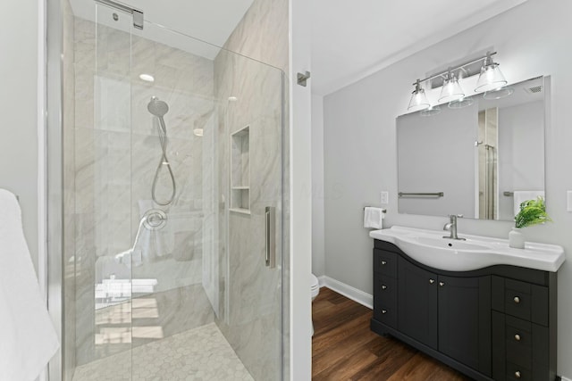 full bath featuring wood finished floors, toilet, vanity, a marble finish shower, and baseboards