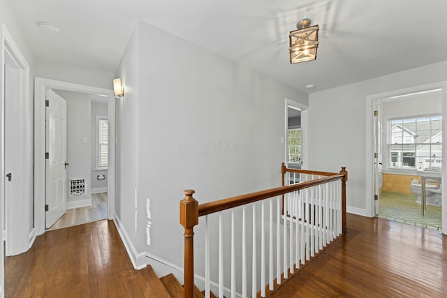 corridor featuring baseboards, a wealth of natural light, an upstairs landing, and wood-type flooring