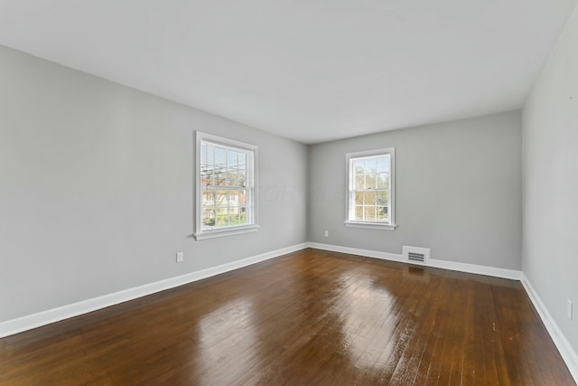 unfurnished room featuring baseboards, visible vents, and dark wood finished floors