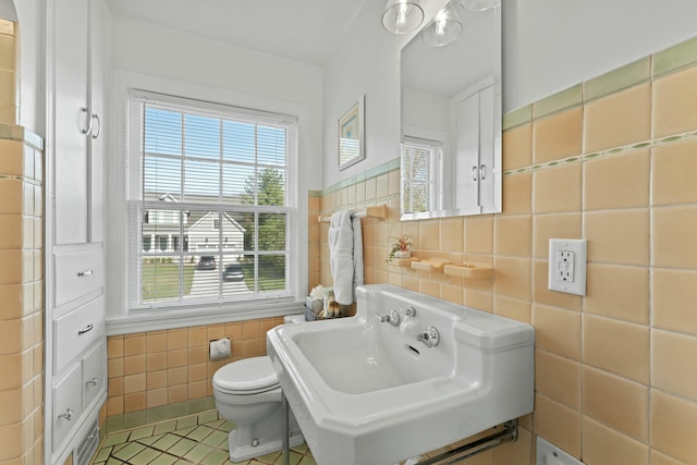 bathroom featuring a sink, toilet, tile patterned floors, and tile walls