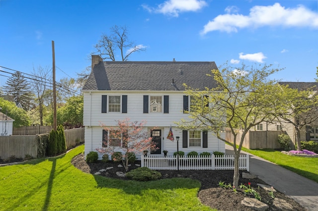 view of front facade featuring fence private yard, roof with shingles, a chimney, and a front yard