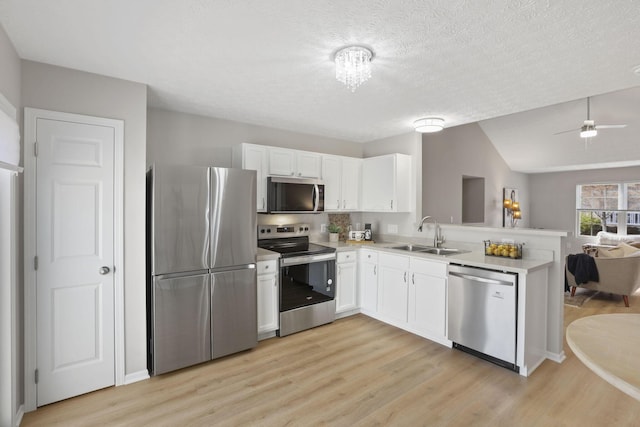 kitchen with white cabinets, a sink, open floor plan, appliances with stainless steel finishes, and a peninsula