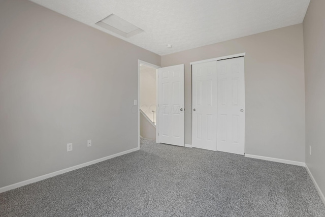 unfurnished bedroom featuring a closet, baseboards, carpet, a textured ceiling, and attic access