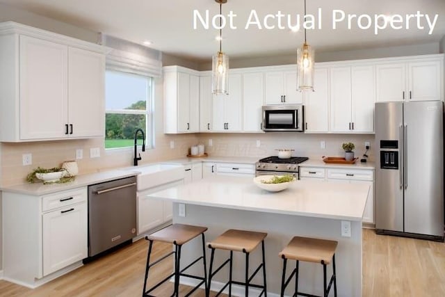kitchen with white cabinets, light wood finished floors, stainless steel appliances, a kitchen island, and a breakfast bar area