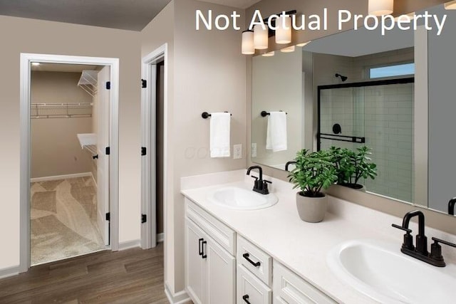 full bathroom featuring a shower stall, wood finished floors, a sink, and a walk in closet
