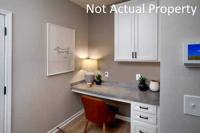 office area featuring built in desk, baseboards, and wood finished floors