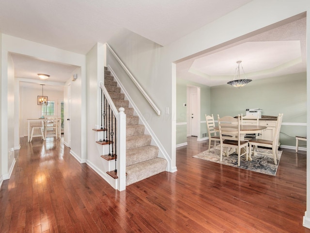 interior space featuring baseboards, a notable chandelier, hardwood / wood-style flooring, a tray ceiling, and stairway