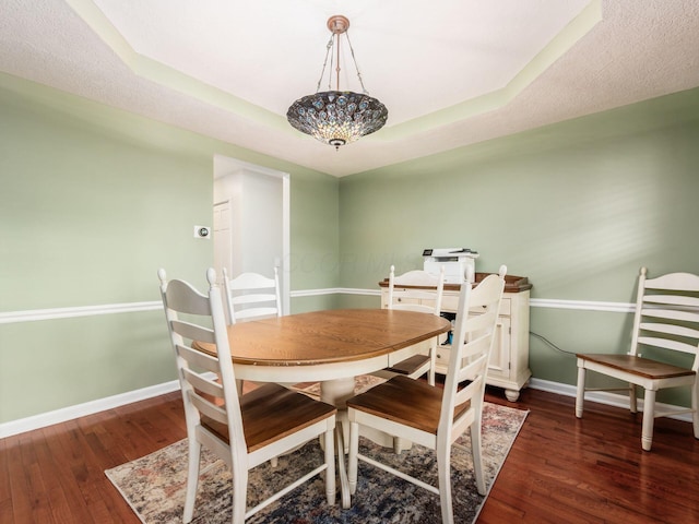 dining space with a raised ceiling, wood finished floors, and baseboards