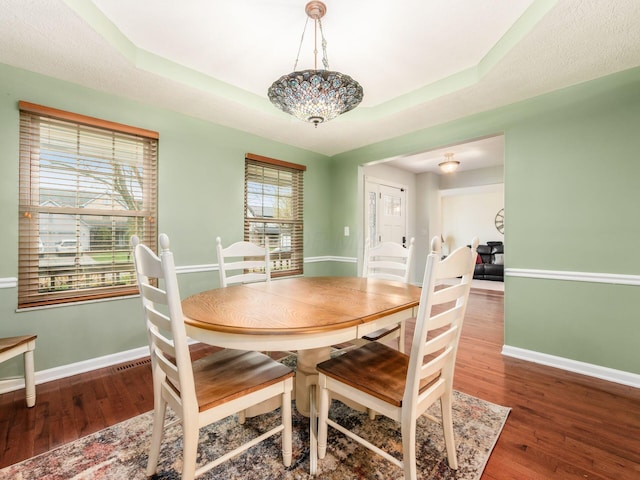 dining room with a tray ceiling, baseboards, and wood finished floors