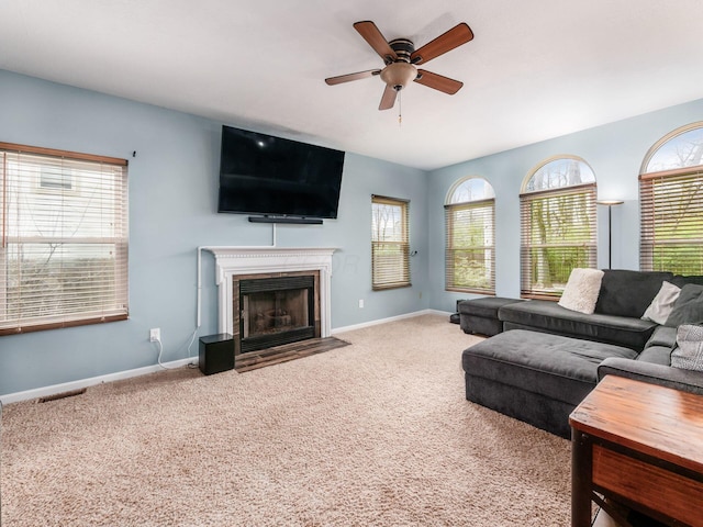 carpeted living room featuring visible vents, ceiling fan, a fireplace with flush hearth, and baseboards