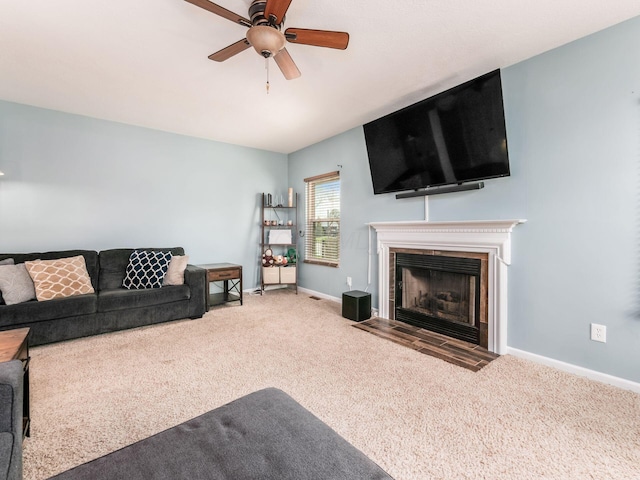 living room with a fireplace with flush hearth, carpet, baseboards, and ceiling fan