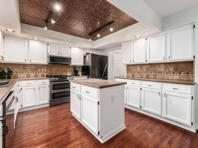 kitchen featuring rail lighting, dark wood-type flooring, appliances with stainless steel finishes, a raised ceiling, and an ornate ceiling