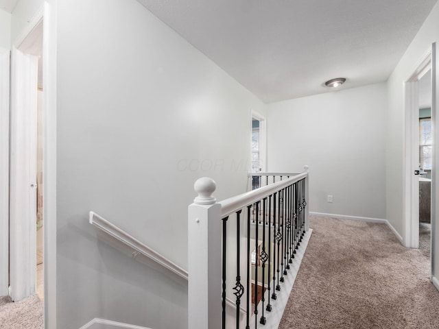 hallway with baseboards, an upstairs landing, and carpet flooring