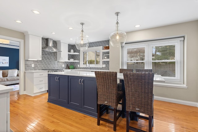 kitchen featuring light countertops, light wood-type flooring, baseboards, white cabinets, and wall chimney exhaust hood