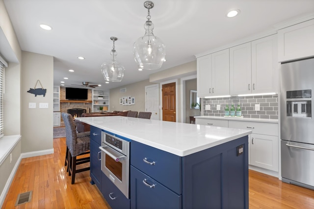 kitchen with white cabinets, light wood finished floors, appliances with stainless steel finishes, and blue cabinets