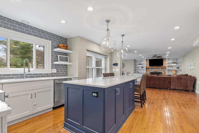 kitchen with light countertops, stainless steel dishwasher, a sink, decorative backsplash, and a large fireplace