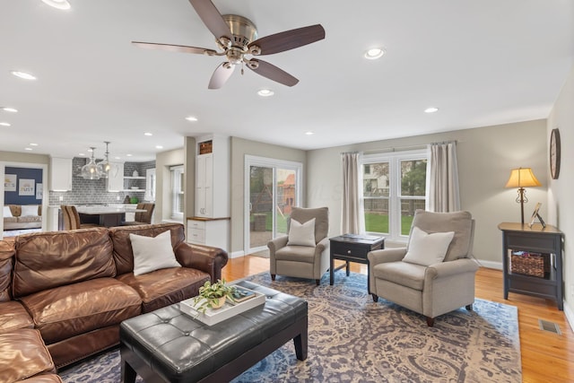 living area with light wood finished floors, baseboards, visible vents, and ceiling fan with notable chandelier