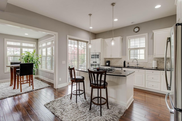 kitchen featuring a kitchen bar, dark wood-type flooring, appliances with stainless steel finishes, a sink, and decorative backsplash